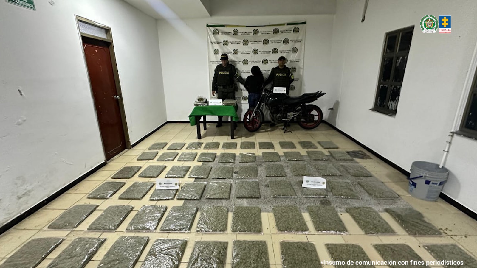 La capturada se encuentra de espalda y custodiada por dos uniformados de la Policía Nacional. En la foto se ve de fondo un backing de la Policía Nacional y el estupefaciente incautado.