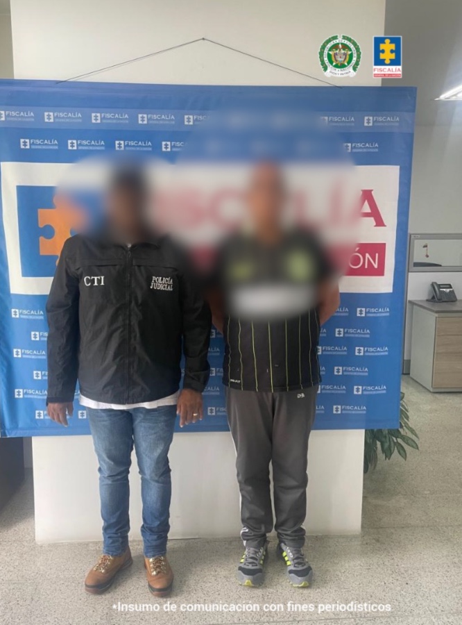 En la imagen está el procesado y un funcionario del CTI con el rostro distorsionado y en la parte de atrás un pendón azul de la Fiscalía General de la Nación