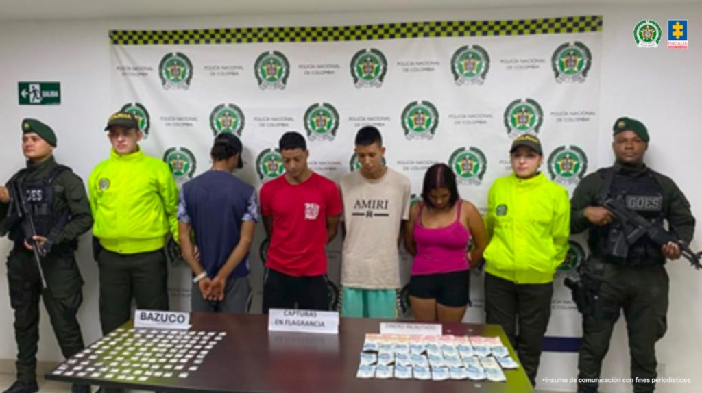 En la fotografía se aprecian de pie a Edilson Andrés Cocuy Herrera, Branyanner Yairuzca García Vizcaya y Juan David Cucuy Galeano. La mujer viste blusa de tiras al cuerpo, de color rojo y short de color negro. Otro, viste de camiseta de color beage, de manga corta con estampado de color negro a la altura del pecho que dice: ‘Amiri’ y usa pantalón de color verde. El otro hombre viste camiseta de color rojo con el escudo de un equipo de fútbol enel lado izquierdo del pecho; pantalón negro. A los extremos de ellos hay uniformados de la Policía Nacional. Delante de ellos hay una superficie de color marrón y sobre ella hay bolsas transparentes pequeñas con contenido de color blanco y dinero en efectivo. Detrás hay un pendón institucional de la Policía.