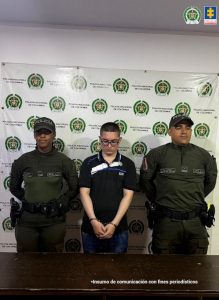 En la fotografía aparece de pie, con los brazos atrás y esposado Edinson Jhoany Zapata Madrid. Viste con camisa de color negro y franja blanca, inclinada, a la altura del pecho; con cuello y jean azul oscuro. Usa lentes de montura negra. En sus extremos hay uniformados de la Policía Nacional. Detrás de ellos hay un pendón institucional de la Policía.