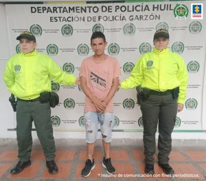 en la imagen se ve un hombre detenido bajo custodia de dos uniformados de la Policía Nacional. Detrás suyo un backing institucional.