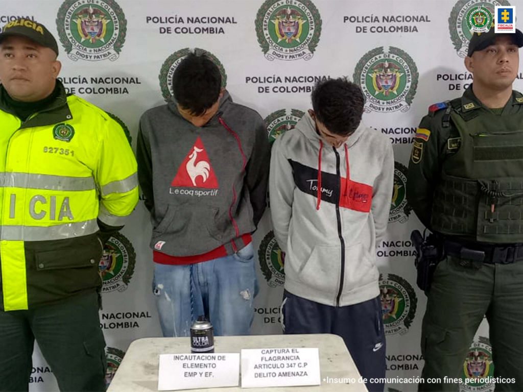 En la foto están los dos hombres capturados con un funcionario de la Policía Nacional a cada lado y en una mesa un frasco de aerosol incautado.