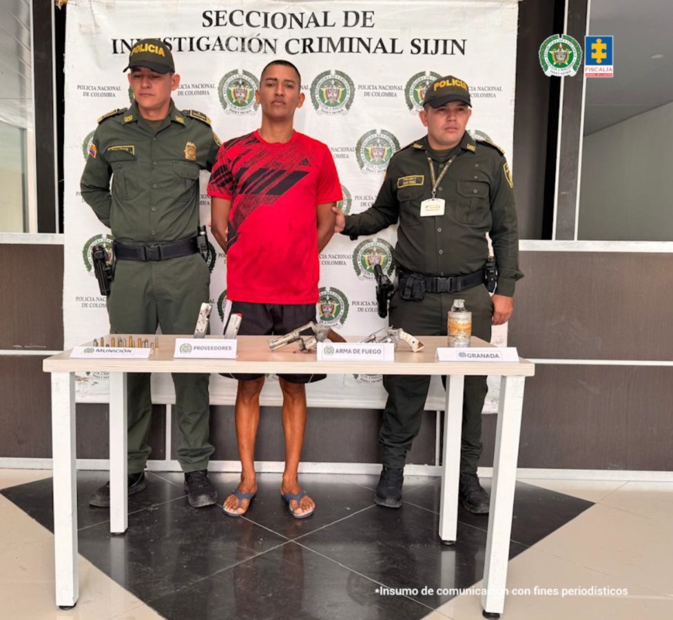 Se visualiza al capturado junto a dos uniformados de la Policía Nacional. Frente a ellos una mesa con los elementos incautados. Detrás de ellos el banner que identifica a la Policía Nacional.