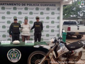 Capturado custodiado por dos policías uniformados. Delante de ellos una mesa con el material incautado y la motocicleta. Detrás banner de la Policía