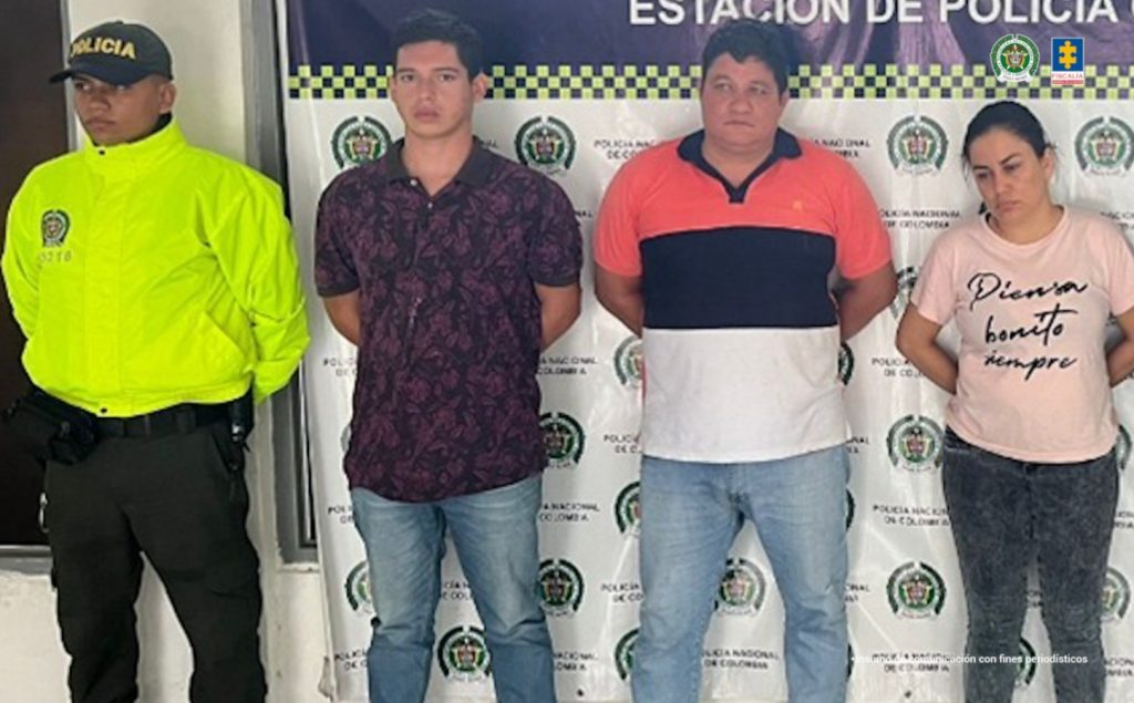 Los imputados se encuentra en custodia por un uniformado de la Policía Nacional. Detrás se observa un backing de la Policía Nacional.