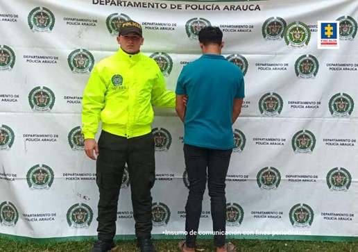 Se observa al capturado de espaldas junto a uniformado de la Policía Nacional. Detrás el banner que identifica al Departamento de Policía de Arauca,