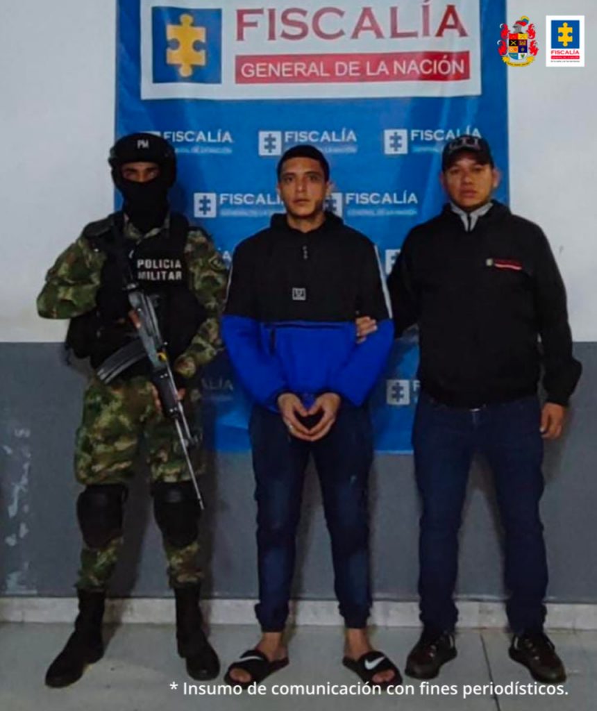 La fotografía muestra al capturado en compañía de un uniformado de la Policía y del Ejército Nacional. Al fondo se ve un backing azul con el logotipo oficial de la Fiscalía. Esta persona es investigada como presunto autor del delito de homicidio.