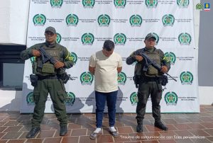 Se visualiza al capturado junto a dos uniformados de la Policía Nacional. Detrás de ellos el banner que identifica a la Policía Nacional. 