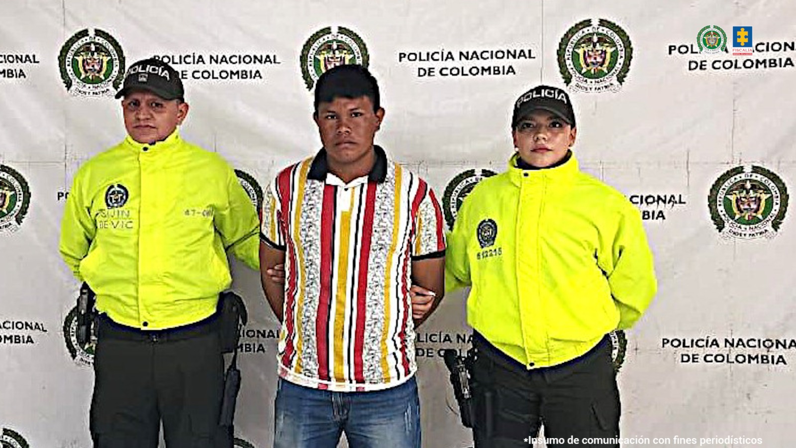 El capturado viste una camisa de rayas de colores, y está esposado con sus manos a la espalda, acompañado de dos uniformados de la Policía Nacional.