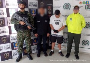Se visualiza al capturado junto a un investigador del CTI y uniformados del Ejército y Policía Nacional. Detrás de ellos los banners del Ejército y Policía Nacional. 