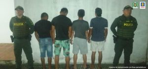 están los capturados de espaldas     custodiados por dos policías. 