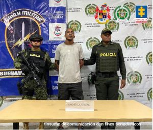 En la fotografía se aprecia de pie y con los brazos atrás a Emerson Ayobi Rentería. Viste con camiseta de color gris claro, con estampado blanco a la altura del pecho; así como pantalón negro. A su extremo derecho hay un uniformado del Ejército Nacional y al izquierdo un uniformado de la Policía Nacional. Delante de ellos hay una superficie y sobre ella hay un letrero que dice: ‘Orden judicial’. Detrás de ellos hay dos pendones institucionales del Ejército y de la Policía.
