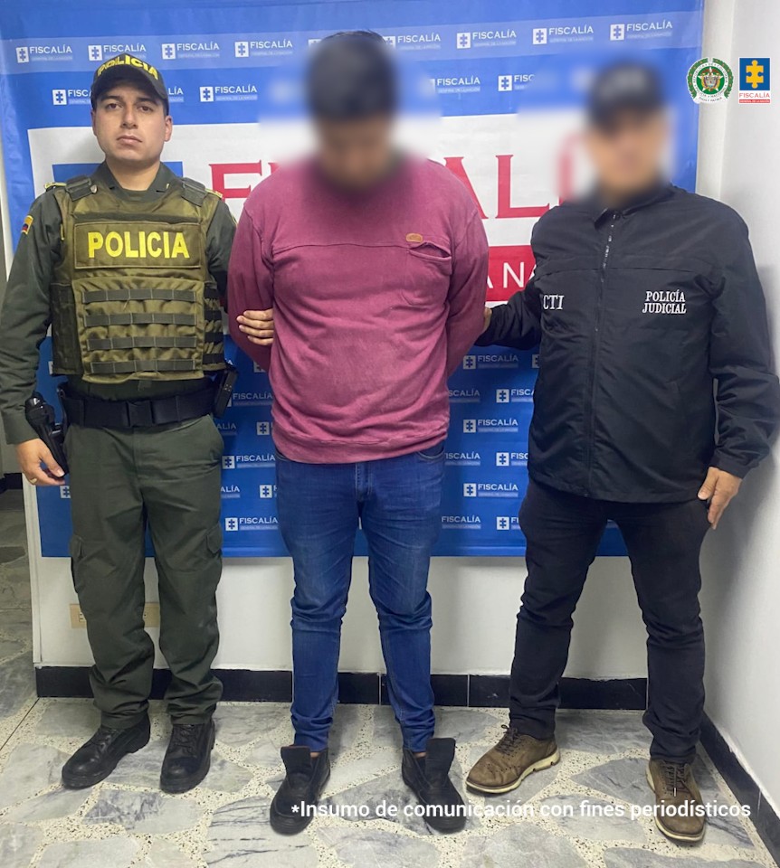En la fotografía aparece de pie, con los brazos atrás y la cabeza inclinada hacia el piso el hoy condenado. Viste con camibuso de manga larga, de color morado, jean azul y zapatillas negras. A su extremo izquierdo hay un servidor del CTI de la Fiscalía y al derecho un uniformado de la Policía Nacional. Detrás de ellos hay un pendón institucional de la Fiscalía.