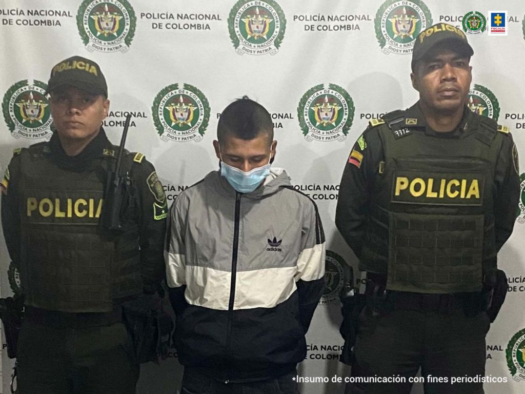 En la fotografía aparece de pie y con los brazos atrás Erick Santiago Montoya Mosca. Viste chaqueta de sudadera con colores gris, blanco y negro y pantalón oscuro. Asimismo usa tapabocas. A lado y lado de él hay uniformados de la Policía Nacional. Detrás de ellos hay un pendón institucional de la Policía.