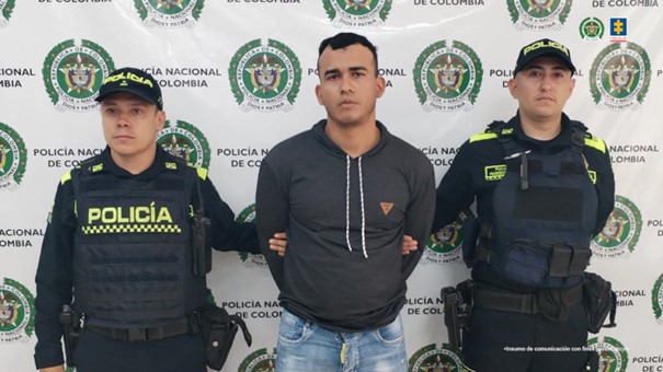 Se visualiza al capturado junto a dos uniformados de la Policía Nacional. Detrás de ellos el banner que identifica a la Policía Nacional.