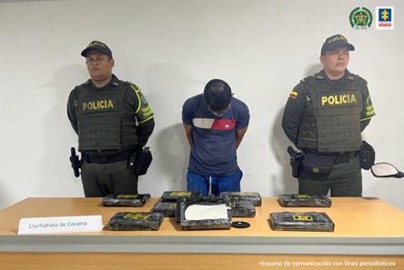 En la fotografía se observa el capturado junto a dos uniformados de la Policía Nacional, al frente de ellos una mesa con 10 paquetes encintados equivalentes a 9.5 kilos de clorhidrato de cocaína