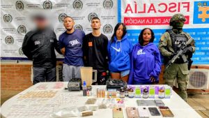 En la fotografía aparecen los cuatro detenidos junto a un servidor del CTI y un uniformado de la Policía Nacional. En la parte superior están un banner de la Fiscalía General y otro banner de la Policía Nacional