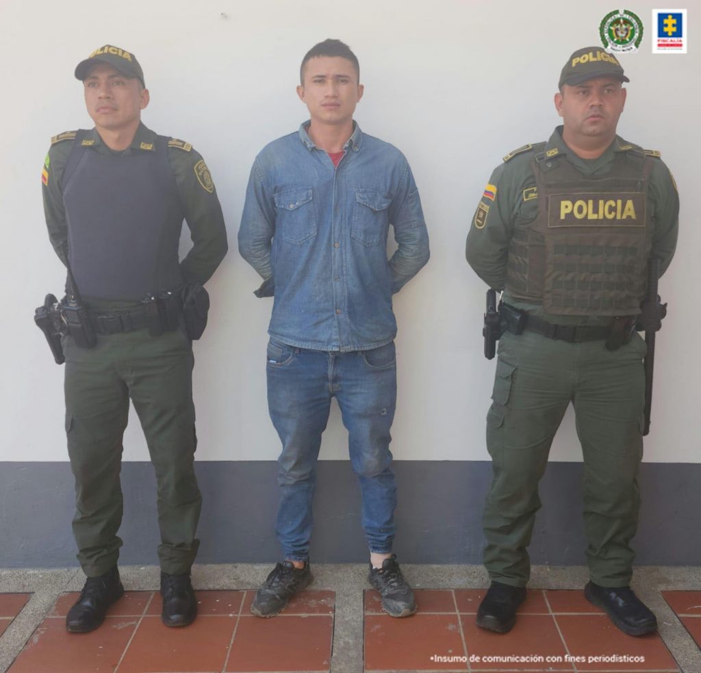 está en capturado esposado con las manos atrás custodiado por dos uniformados de la Policía Nacional.