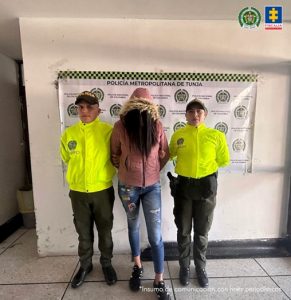 Se visualiza a la capturad junto a dos uniformados de la Policía Nacional. Detrás de ellos el banner que identifica a la Policía Nacional.