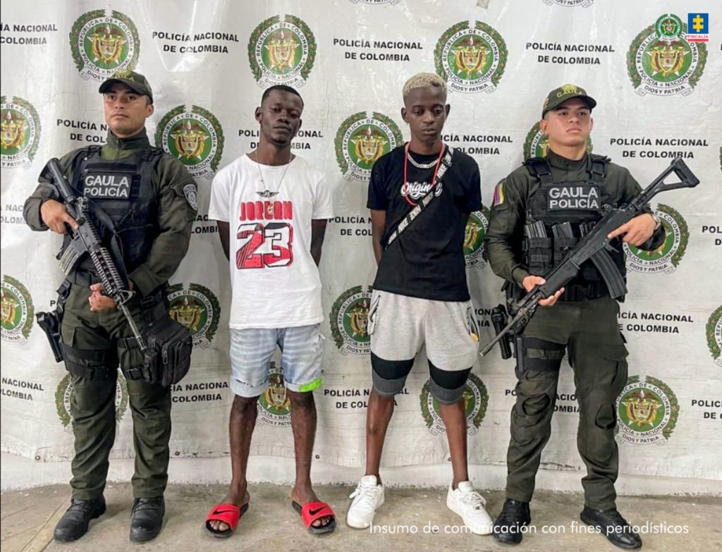 En la fotografía aparecen los dos capturados junto a dos uniformados de la Policía Militar. En la parte superior está un banner de la Policía Nacional.