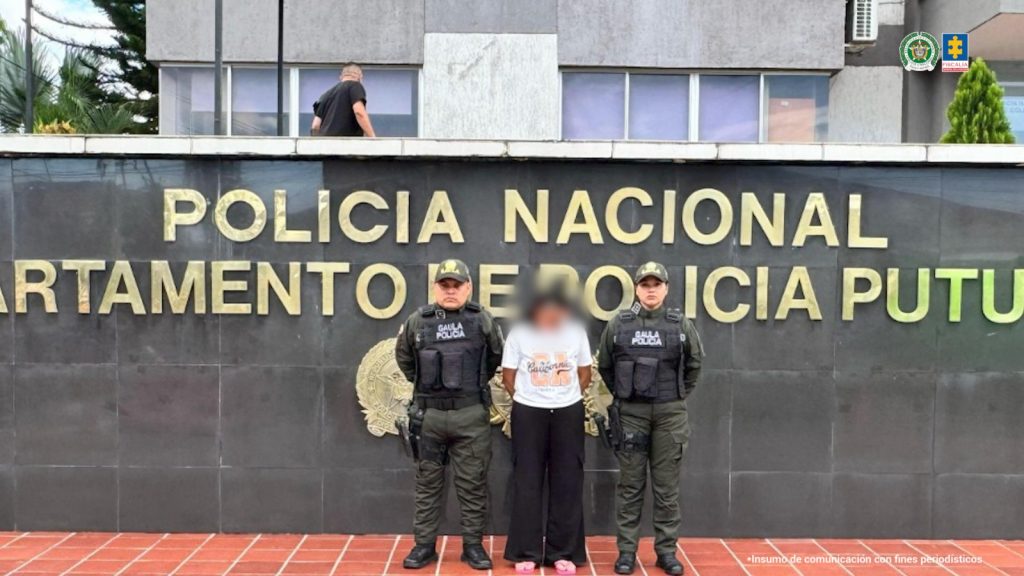 La capturada se encuentra de frente y custodiada por uniformados del Gaula de la Policía Nacional. Detrás se observa un mural con el letrero del Departamento de Policía Nacional Putumayo .