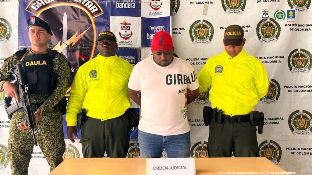 En la fotografía aparece el capturado junto a un integrante de la Policía Nacional y un soldado del Gaula Militar. En la parte superior están un banner del Gaula Militar y un banner de la Policía Nacional.