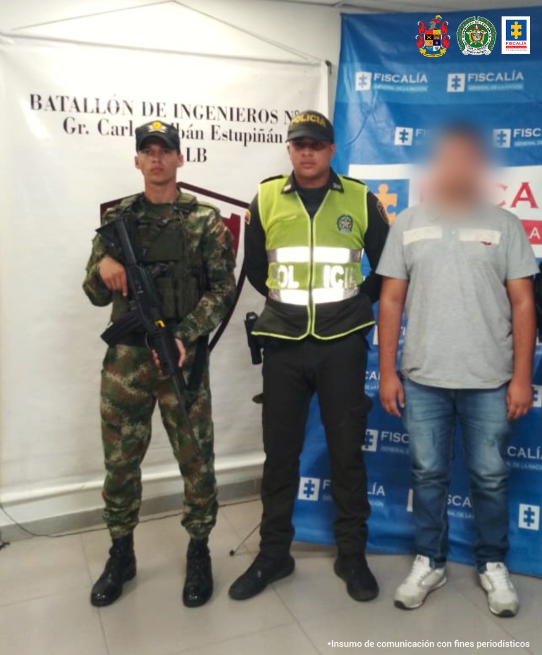 El capturado está custodiado por unidades de la policía y el ejército, detrás de ellos está un pendón institucional de la Fiscalía General de la Nación.