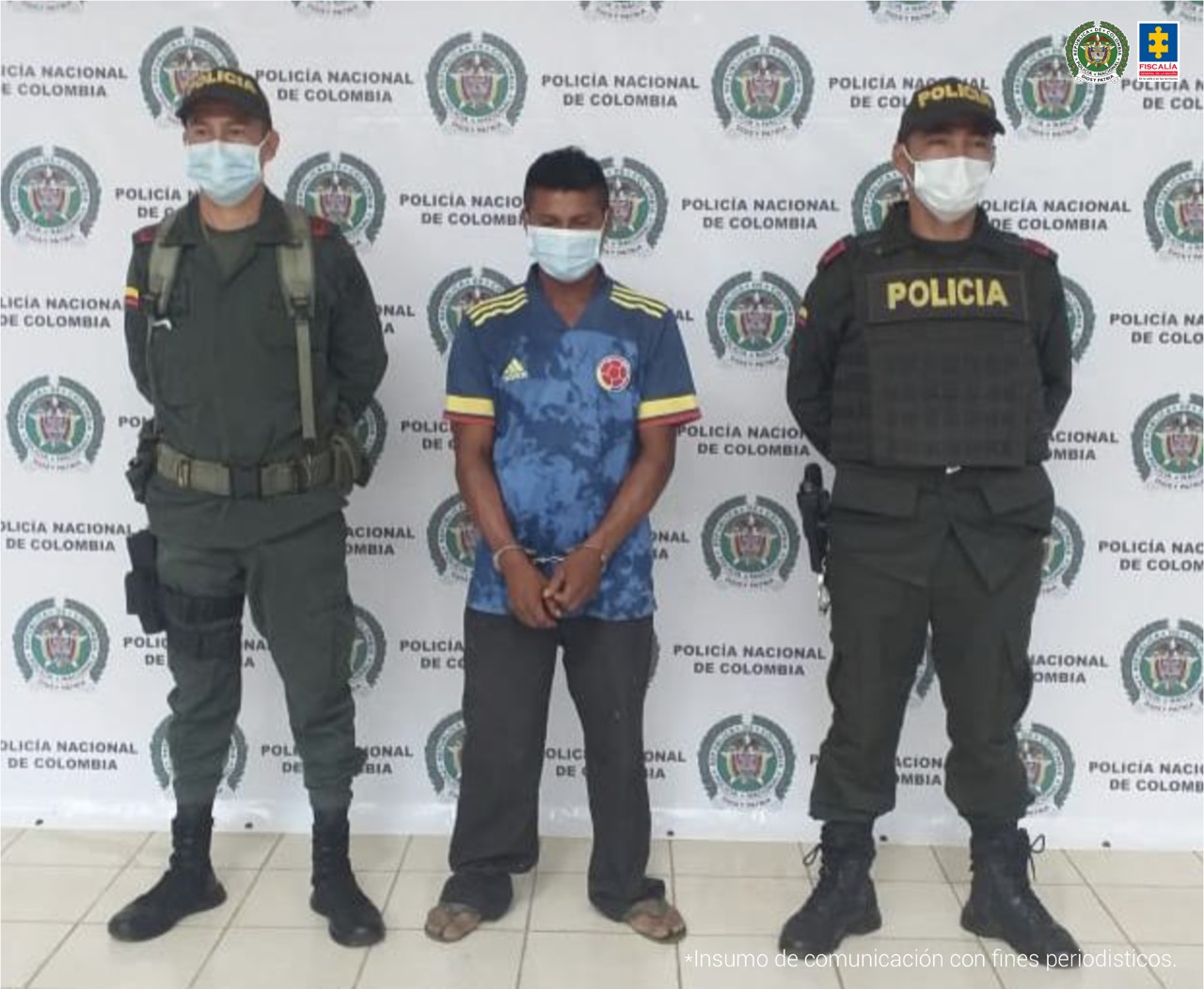 El capturado aparece esposado con sus manos adelante, en medio de dos uniformados de la Policía Nacional y detrás hay un pendón institucional.