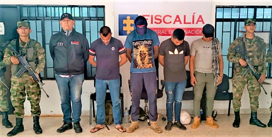 Los cuatro capturados están en medio de servidores del CTI y dos uniformados del Ejército Nacional, detrás de ellos hay un pendón de la Fiscalía General de la Nación.