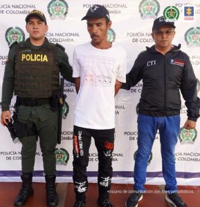 El capturado tiene una camiseta blanca, gorra y está custodiado por un servidor del CTI de la Fiscalía y un uniformado de la Policía Nacional.