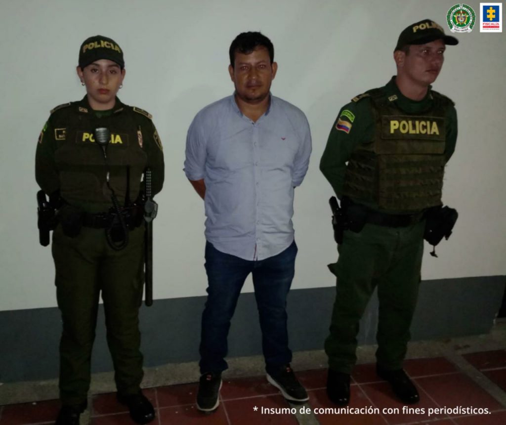 El captuado está esposado con sus manos a la espaclda y está custodiado de dos policías.