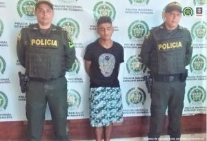 El capturado está rodeado de dos uniformados de la policía nacional, y con las manos esposadas, de fondo hay un pendón institucional.