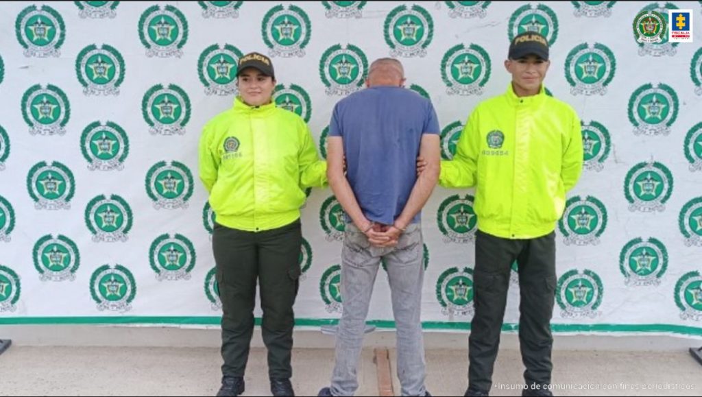 El capturado aparece de espalda, con sus manos esposadas y custodiado por miembros de la policía nacional.