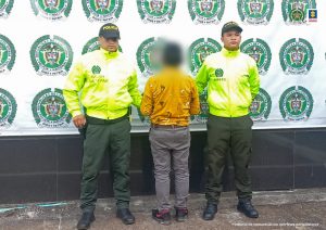 El hombre aparece de espalda a la cámara, está esposado con sus manos al frente y custodiado por uniformados de la policía nacional