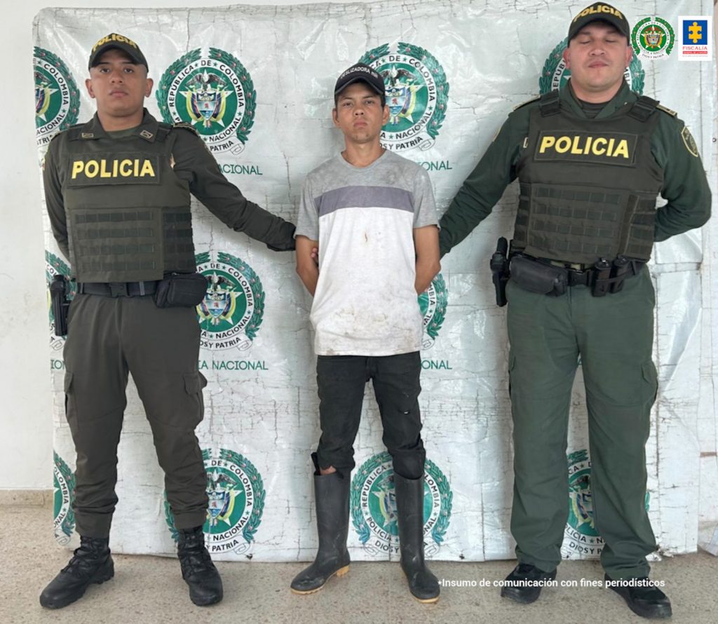 El capturado está esposado y custodiado por dos hombres de la policia nacional.