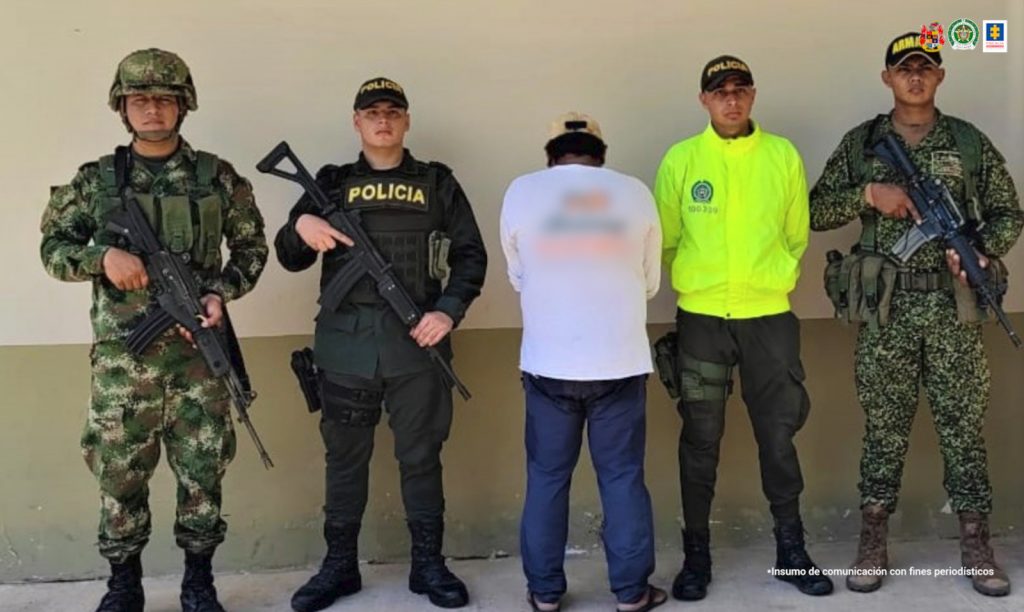 El hombre aparece de espalda a la cámara y está custodiado por miembros del ejército, policía nacional y armada nacional.
