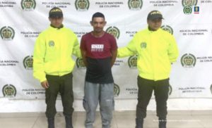 El condenado, está esposado a su espalda y lo tiene sujetado dos uniformados de la Policía Nacional, detrás de ellos, está un pendón de la institución.