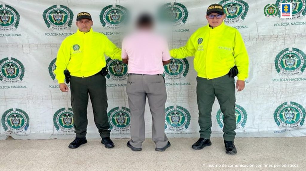 El captuado está de espalda, tiene sus mabnos esposadas y está custodiado por dos uniformados de la policía nacional.