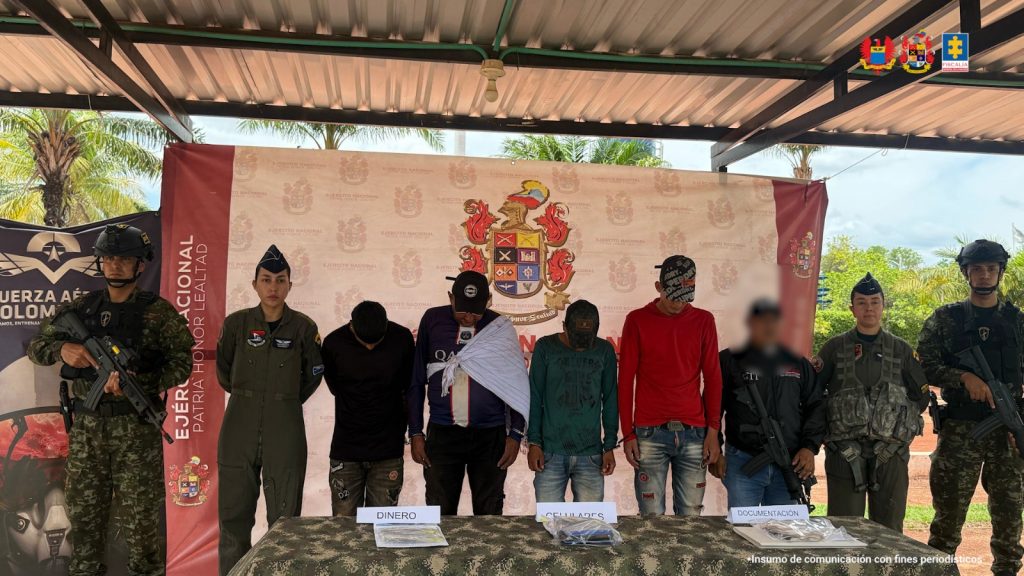 Los capturados están esposados, y están custodiados por uniformados del Ejército, la Fuerza Aérea Colombiana y CTI de la Fiscalía. En una mesa frente a ellos, aparecen los elementos incautados como dibnero en efectivo, talonarios de cobro y equipos de comunicación.