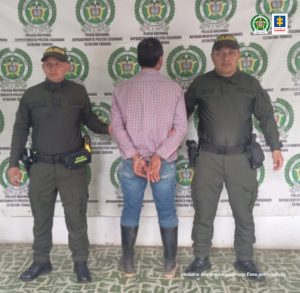 El capturado aparece de espalda y custodiado por uniformados de la Policía Nacional.