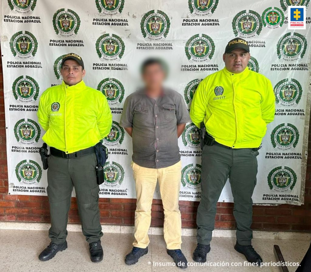 El capturado tiene puesta una chaqueta, está esposado con sus manos al frente y está custodiado por dos uniformados de la policía nacional.
