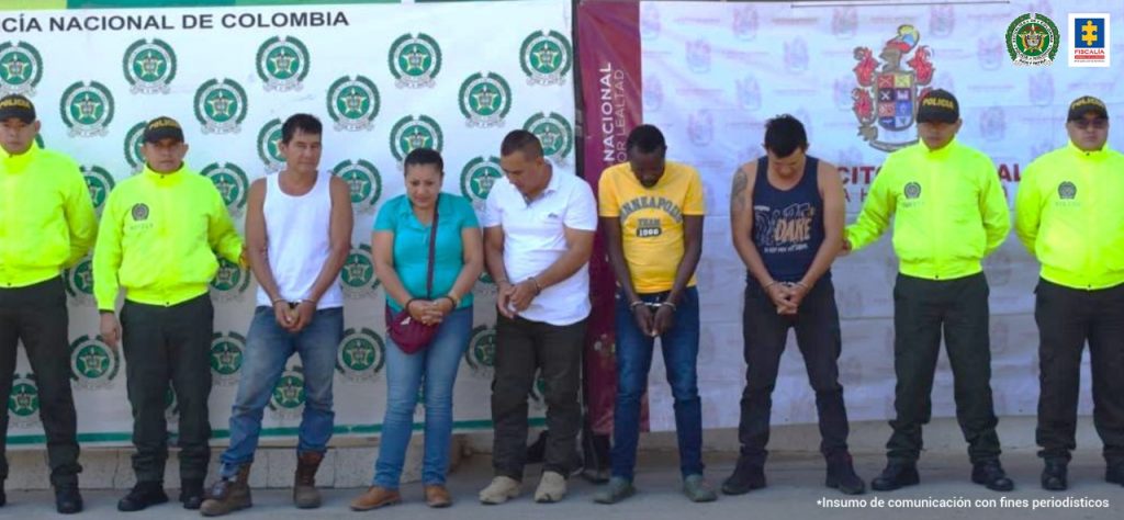Los capturados, una mujer y cuatro hombres, están custodiados por efectivos de la Policía Nacional. Están esposados con las manos al frente.