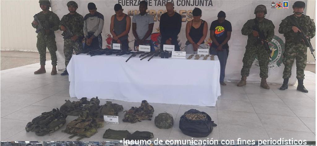 En la fotografía aparecen los 6 capturados junto a dos infantes de la Armada Nacional y dos soldados del Ejército Nacional. En la parte posterior se ve una mesa con fusiles, escopetas, radios de comunicaciones y munición de diferentes calibres