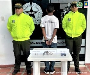 El capturado aparece de espalda a la cámara con sus manos esposadas y custodiado por dos uniformados de la policía nacional.