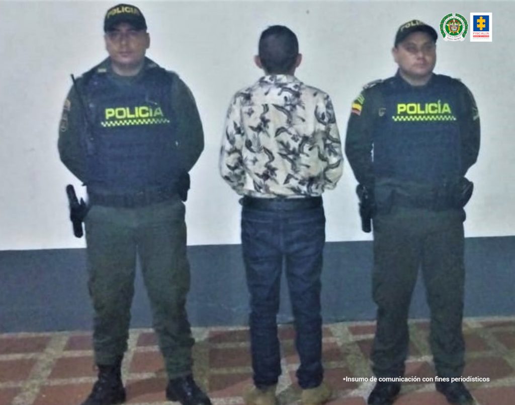 El capturado aparece de espalda a la cámara, está en medio de dos uniformados de la policía y de fondo un pendón institucional.