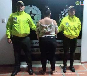 La capturada está esposada con sus manos al frente y de espalda a la cámara, custodiada por dos uniformados de la policía