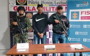 El capturado está custodiado por hombres del CTI de la Fiscalía y Gaula militar, en una mesa frente a ellos, están los elementos incautados tales como un equipo celular, recibo de pago y el dinero incautado.