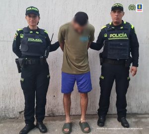 El capturado está con su rostro agachado, y sujetado por dos uniformados de la policía nacional.
