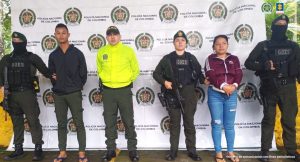 Los capturados están custodiados por uniformados de la policía nacional, esposados y de fondo hay un pendón institucional.