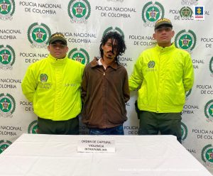 En la fotografía se encuentra el procesado con dos servidores de la Policía Nacional y un pendón de esa institución en la parte de atrás.